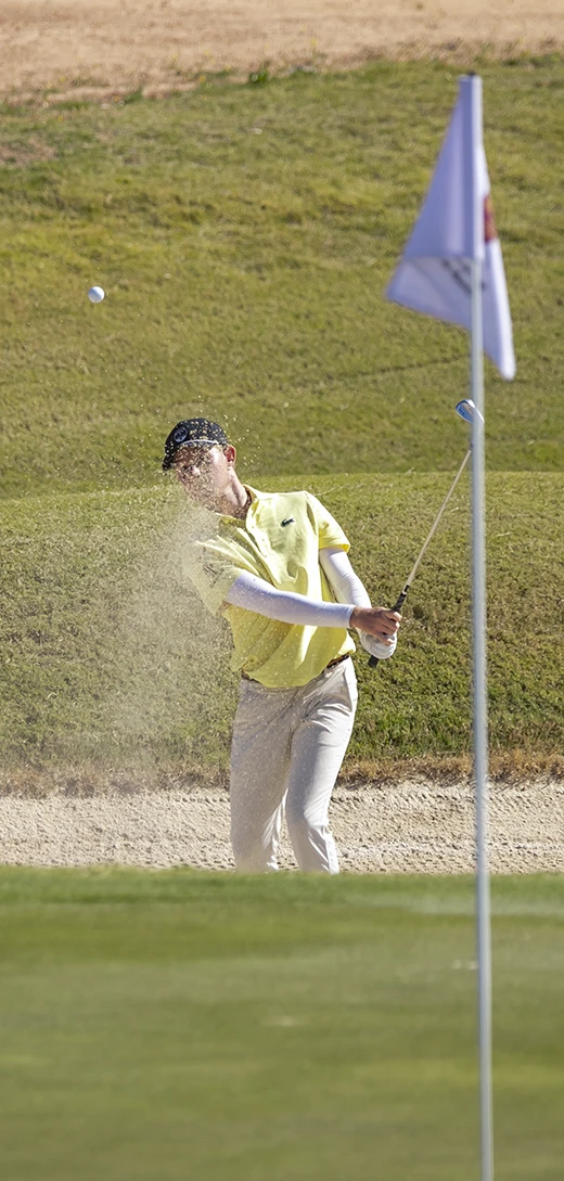 Jugador ejecutando un golpe desde el bunker, arena en suspensión y trayectoria de la bola hacia la bandera en la IV Copa Región de Murcia 2026.